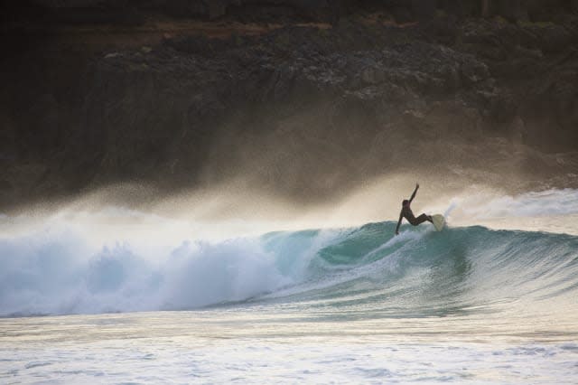 Silhouetted young man surfing wave at sunset, Fuerteventura, Spain