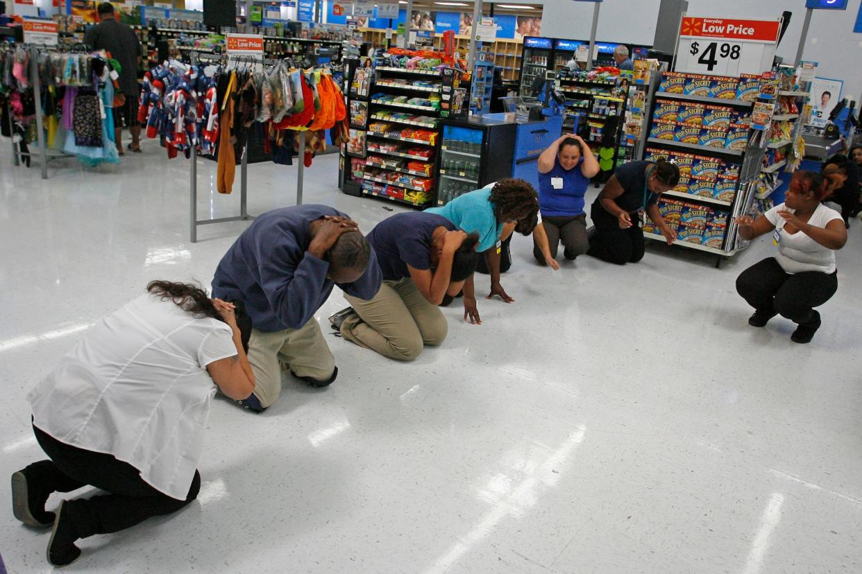 seven people crouch on the floor of a Walmart and cover their heads in an earthquake drill