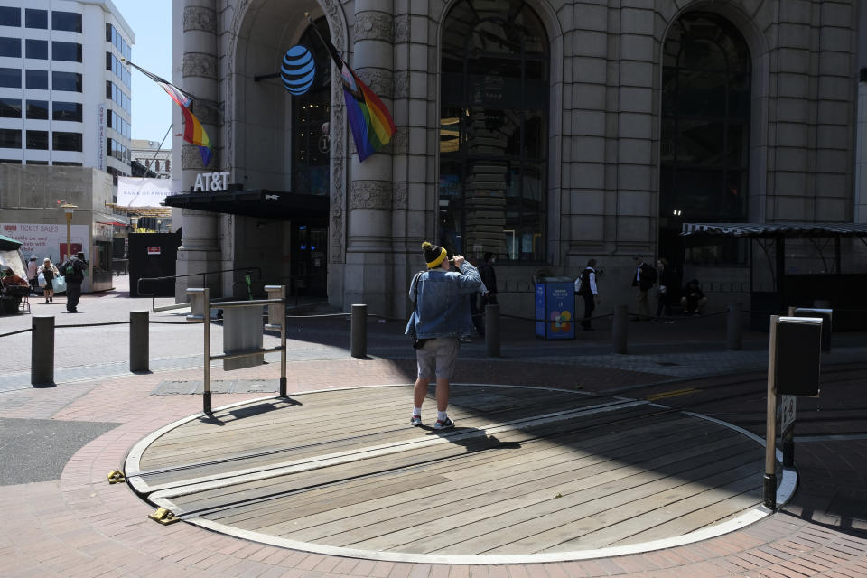 A man vapes on an empty cable car turnaround at Powell and Market streets in San Francisco, on June 21, 2023. In the background is the flagship AT&T store that recently announced it is closing. San Francisco's downtown has seen an exodus of retailers and now a shopping mall owner is turning it over to its lender in the face of declining foot traffic and empty office space. (AP Photo/Eric Risberg)