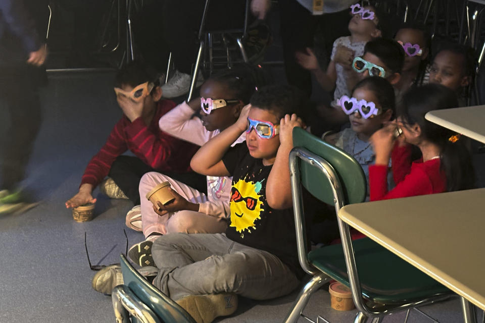 Second-grade student Jose Byrd (black t-shirt with sun) and classmates try out eclipse viewing glasses that they decorated at Riverside Elementary School in Cleveland on March 14, 2024. Teachers in or near the path of totality say they have worked to come up with educational and engaging lessons for the rare event. (AP Photo/Carolyn Thompson)