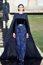 <p>Model wears a long cape over a blue velvet and beaded skirt. (Photo: Getty Images) </p>