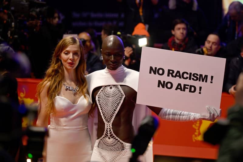 Senegalese model and fashion entrepreneur Papis Loveday (R) stands on the opening night of the Berlinale with a protest sign "No Racism ! No AFD !" next to German actress Pheline Roggan on the red carpet. The 74th Berlin International Film Festival will take place from February 15 - 25, 2024. Monika Skolimowska/dpa