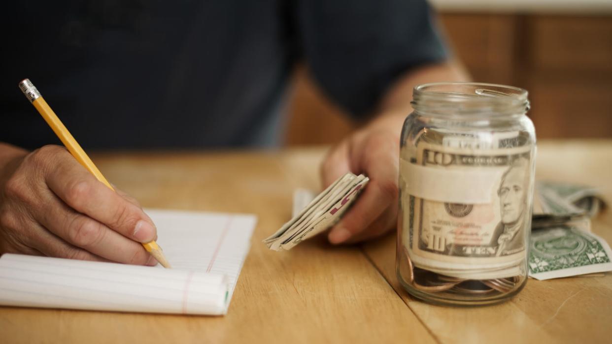 A male writes notes concerning money at the kitchen table.