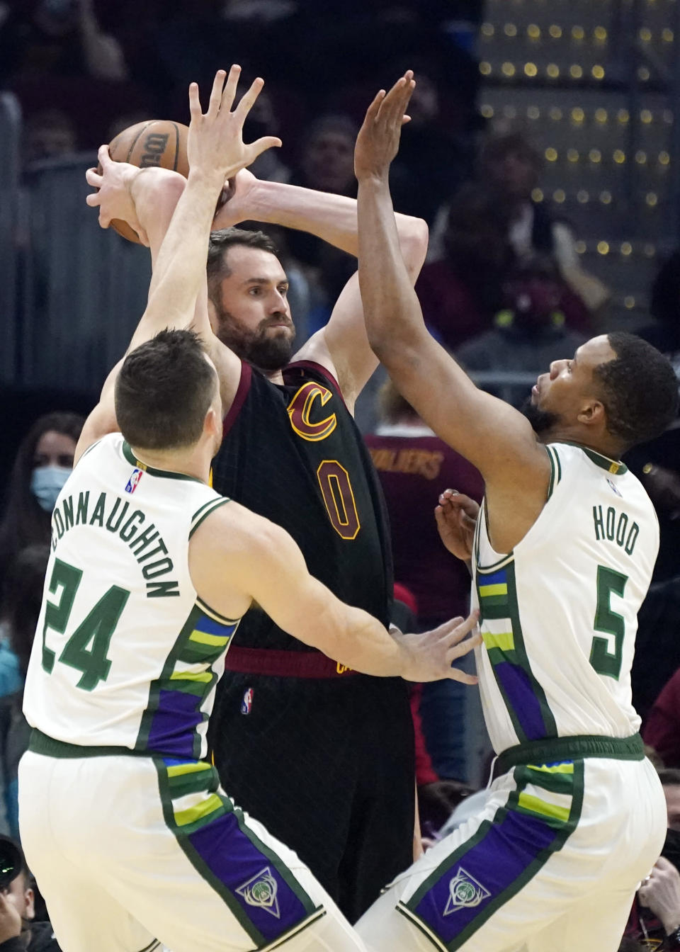 Cleveland Cavaliers' Kevin Love, center, passes as Milwaukee Bucks' Pat Connaughton, left, and Rodney Hood defend in the first half of an NBA basketball game, Wednesday, Jan. 26, 2022, in Cleveland. (AP Photo/Tony Dejak)