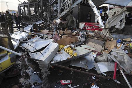 People gather around wreckage after a car bomb at a bus station in Soumariya, near Damascus November 26, 2013, in this handout picture released by Syria's national news agency SANA. REUTERS/SANA/Handout via Reuters