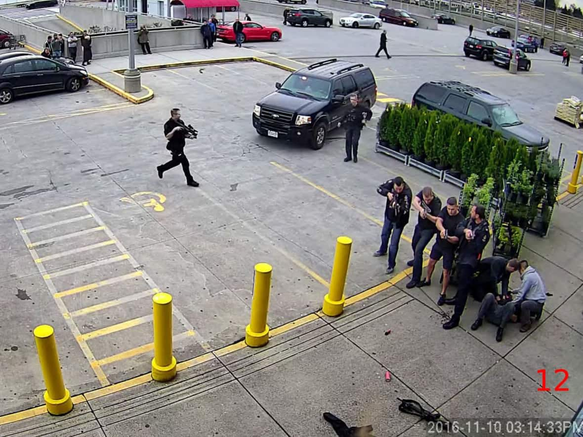 In this image taken from surveillance footage, four Vancouver police officers can be seen aiming their firearms at Daniel Peter Rintoul outside a Canadian Tire on Nov. 10, 2016. A police service rifle lies between the officers and an injured Rintoul, who is out of frame on the bottom right. To the right, two officers attend to Const. Justin Fraser's stab wounds. (B.C. Coroners Service - image credit)