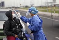 A nurse from the Ministry of Public Health takes a sample from a person on a motorcycle, at a new coronavirus mobile test site in Asuncion, Paraguay, Wednesday, April 8, 2020. The government of Paraguay has announced the extension of the quarantine for one week until April 21. (AP Photo/Jorge Saenz)