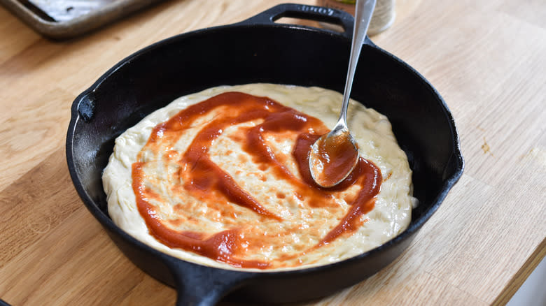 spreading tomato sauce on pizza