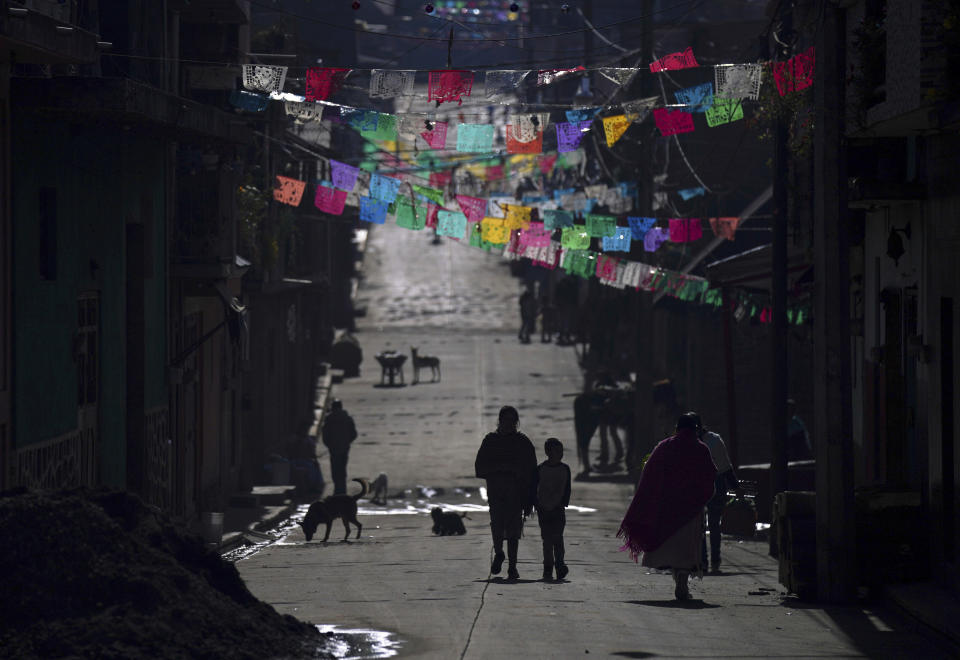 Residents walk along a street decorated with elaborately cut colored pieces of tissue paper called “papel picado, in the Puerpecha Indigenous community of Comachuen, Mexico, Wednesday, Jan. 19, 2022. Money sent home by migrants working in the United States has allowed their families to remain in Comachuen rather than moving to other parts of Mexico for work. (AP Photo/Fernando Llano)