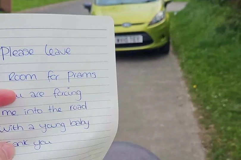 One of Louise's notes held in front of a car, which reads "Please leave room for prams you are forcing me into the road with a young baby, thank you"