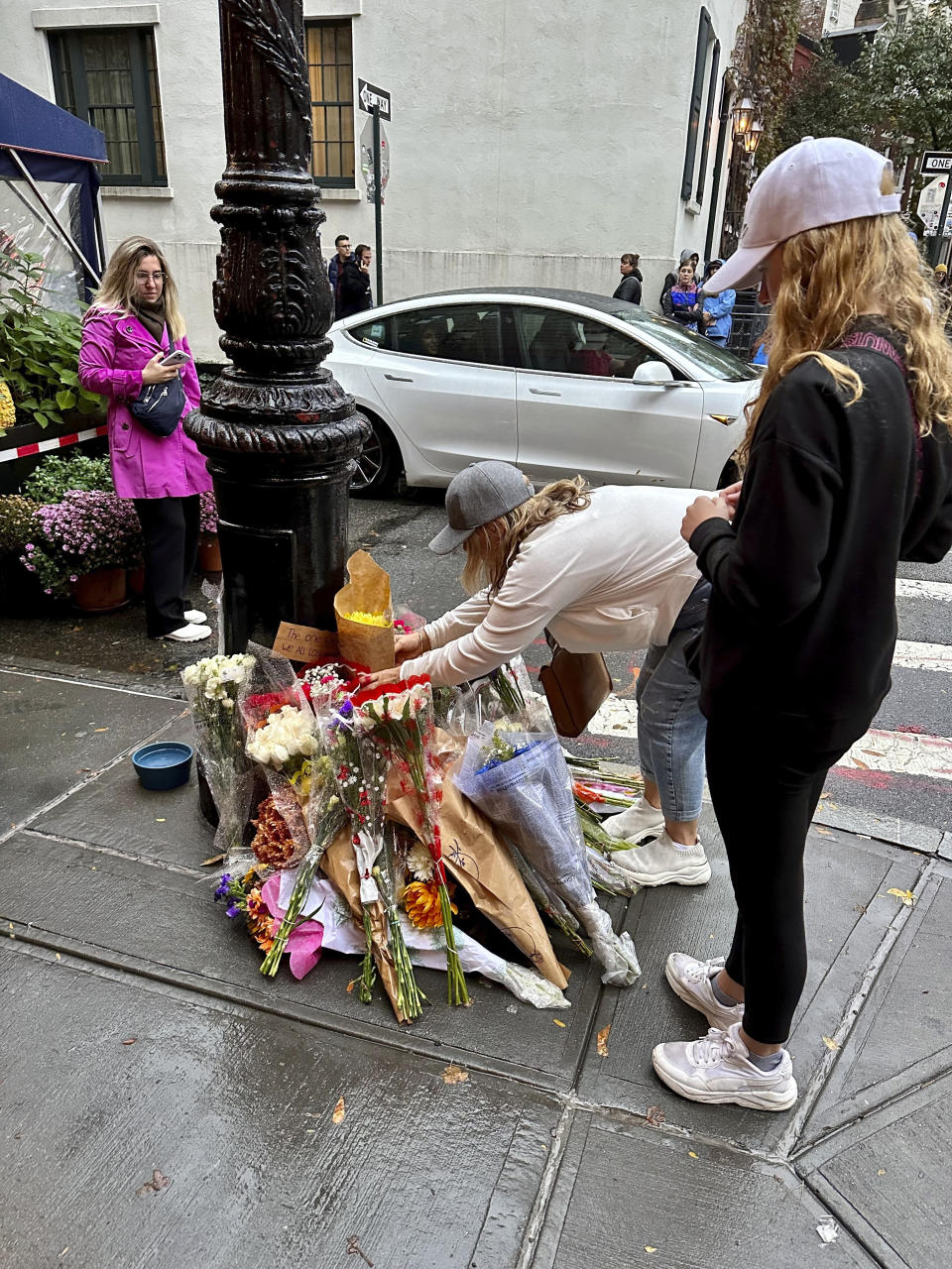 Fans place flowers at a makeshift memorial for Matthew Perry outside the building known as the "Friends" building in New York, Sunday, Oct. 29, 2023. People lingered in the rain, taking pictures and leaving flowers on the corner outside the building shown in exterior shots on the popular TV show. Perry, who played Chandler Bing on NBC’s “Friends” for 10 seasons, was found dead at his Los Angeles home on Saturday. He was 54. (AP Photo/Brooke Lansdale)