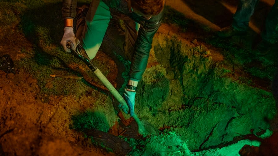 A man uses a shovel to dig a hole in the dark.