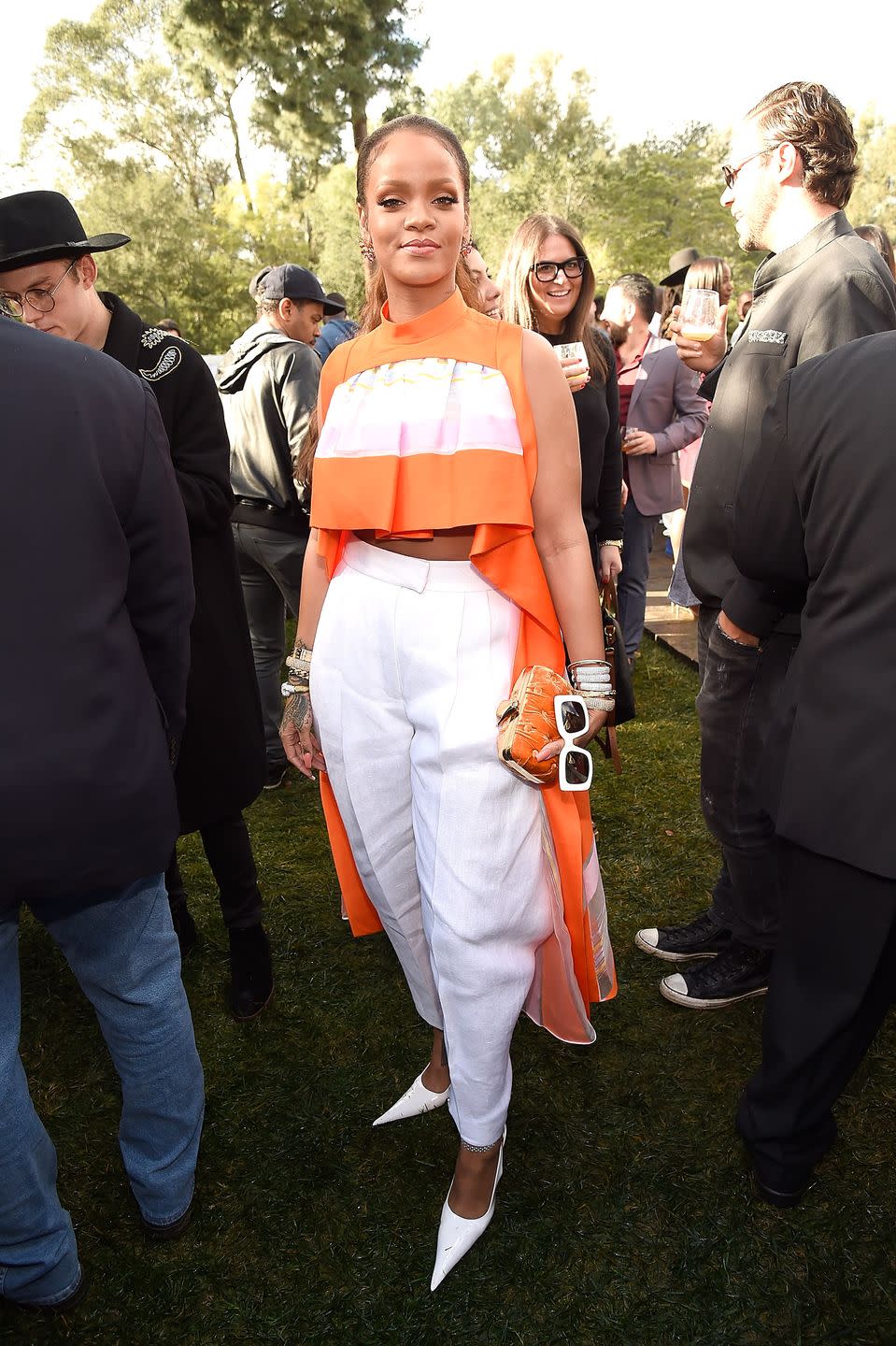 <p>In an orange crop top and white trousers by Delpozo with a tangerine-colored clutch and white pointy-toed pumps. </p>