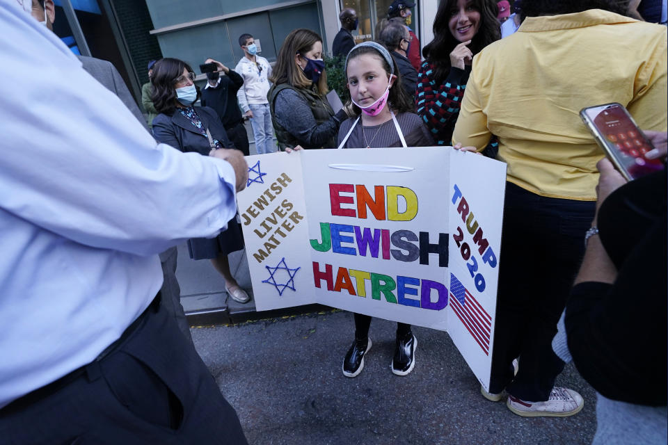 A young girl holds a poster she made as she prepares to pose for a cell phone photograph for a relative as she and others joined protesters outside the offices of New York Gov. Andrew Cuomo, Thursday, Oct. 15, 2020, in New York. Three Rockland County Jewish congregations are suing New York state and Cuomo, saying he engaged in a "streak of anti-Semitic discrimination" with a recent crackdown on religious gatherings to reduce the state's coronavirus infection rate. (AP Photo/Kathy Willens)