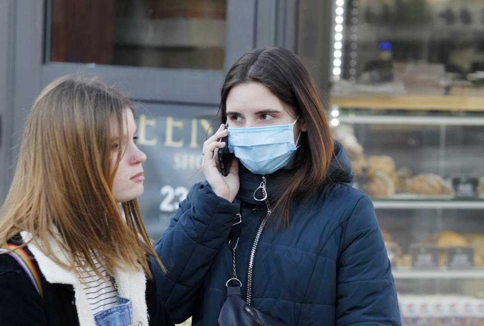 An young woman wearing a protective face mask as a preventive measure against corona virus uses a mobile phone in the street.