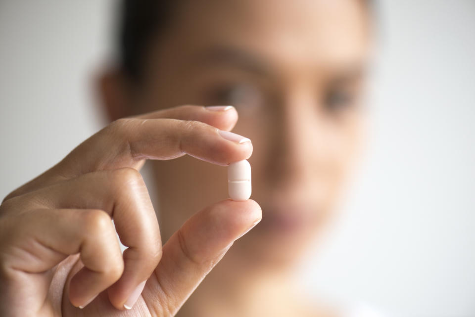 Person holding a capsule between fingers close to camera, partially obscuring face