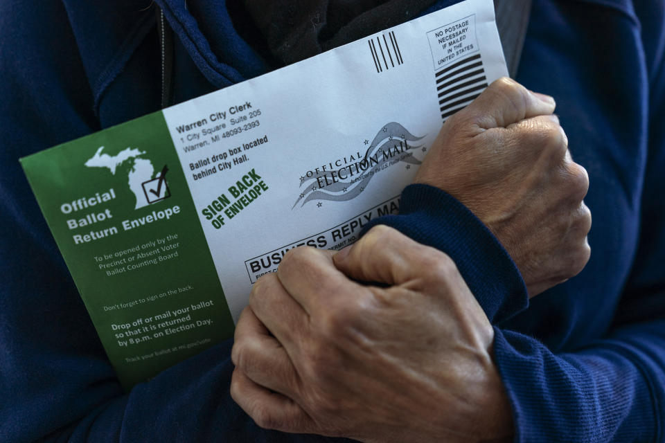 FILE — A Michigan voter clutches her absentee ballot before dropping it off at the city clerk's office in Warren, Mich., on Oct. 28, 2020. A total of 1.6 million people have requested absentee ballots so far this year, surpassing the 1.16 million who chose the option in the 2018 midterm election. (AP Photo/David Goldman, File)