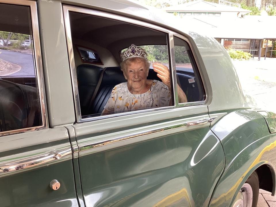 Centenarian Katie MacRae on her 106th birthday in the back of an old car, wearing a tiara.