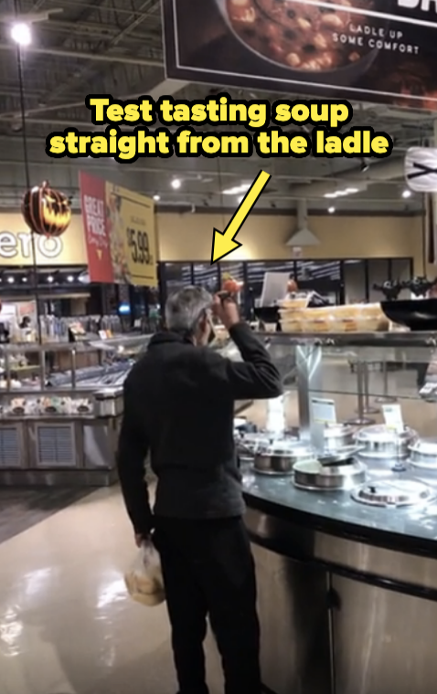 Person test tasting soup straight from the ladle in a grocery store. They are standing next to the soup counter with multiple soup containers