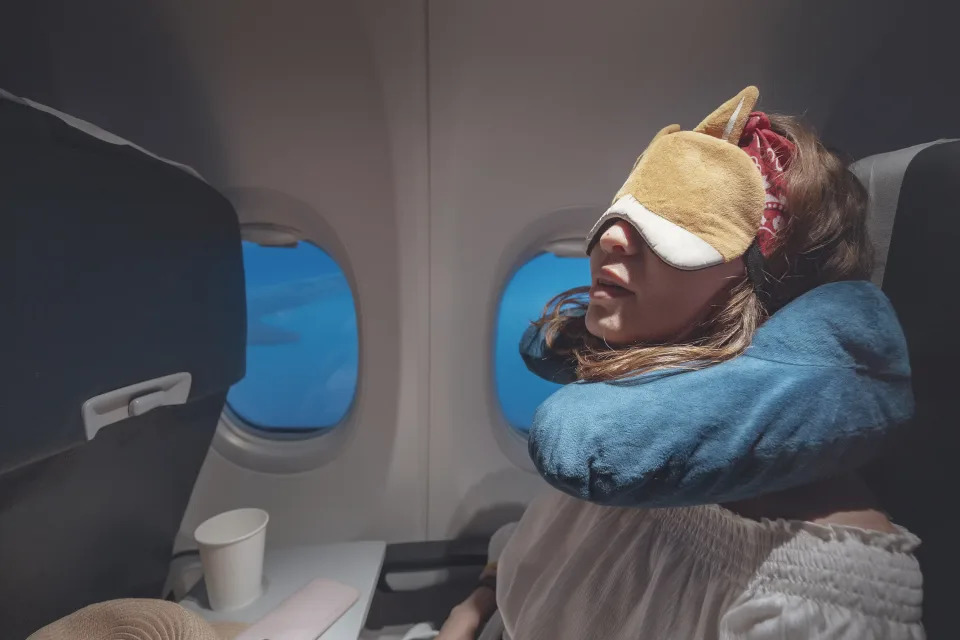 Happy and tired young woman comfortably sleeping with mask and pillow in airplane. Sophisticated traveler concept