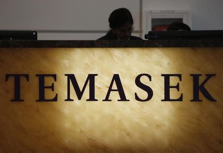 A receptionist stands behind a logo of state investor Temasek Holdings at their office in Singapore July 8, 2014. REUTERS/Edgar Su