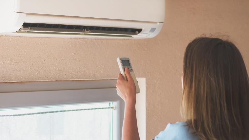 Woman holding remote control aimed at the air conditioner.