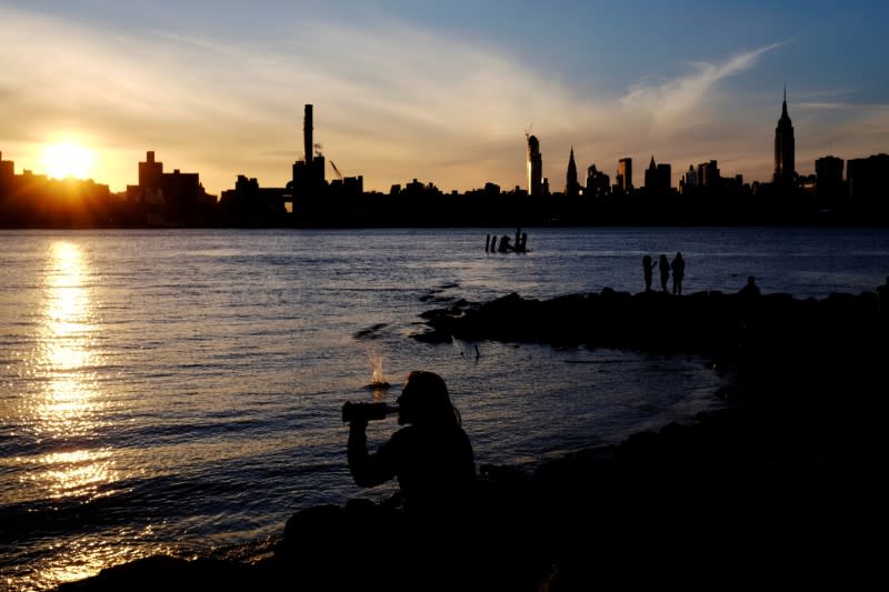 FILE PHOTO: A man drinks beer as he sits by the East River to watch the sunset in the Brooklyn borough of New York