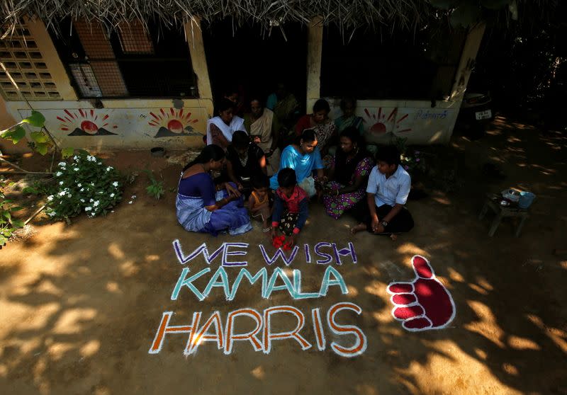 Women and children sit next to a message for U.S. Democratic vice presidential nominee Kamala Harris in Painganadu