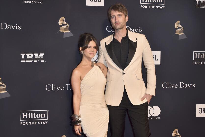 Maren Morris is wearing a beige dress and is standing next to Ryan Hurd who is wearing a beige suit