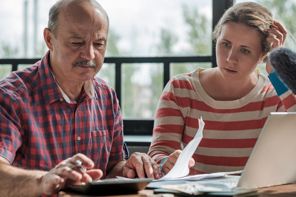 Spanish man counting money with his daughter sitting in the living room. Helping children while retired.