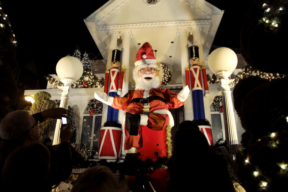 This Dec. 4, 2012 photo shows spectators viewing a a giant Santa Claus at a decorated home in the Brooklyn borough of New York. Each holiday season, tour operator Tony Muia takes tourists from around the world on his “Christmas Lights & Cannoli Tour” visiting the Brooklyn neighborhoods of Dyker Heights and Bay Ridge, where locals take pride in over-the-top holiday light displays. (AP Photo/Seth Wenig)