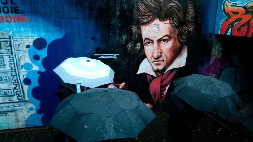 Paraguas de gente que pasa cerca de un grafiti de Beethoven en su ciudad natal de Bonn.