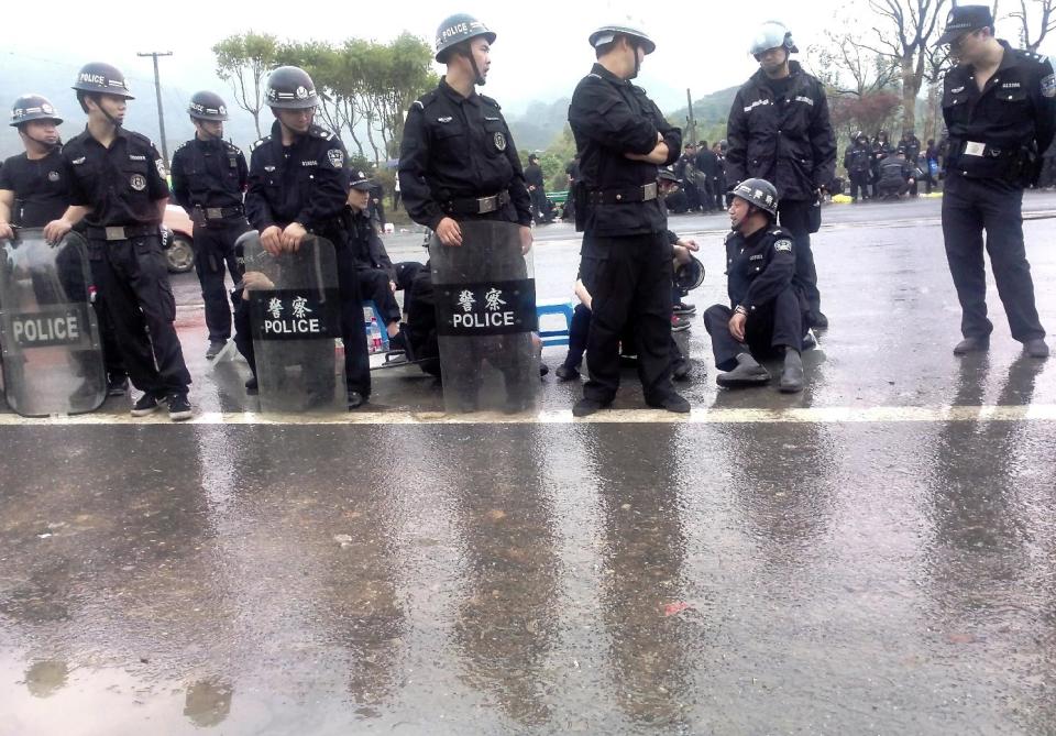 In this Sunday, May 11, 2014 photo released by Hong, Chinese police with shields man during a protest against the construction of a waste incinerator in Yuhang district, Hangzhou in China's Zhejiang province. Government pledges to seek public approval for a planned waste incinerator in eastern China failed to appease the project's neighbors Monday, May 12, 2014 after thousands of them, concerned over potential health hazards, blocked a highway and clashed with police in a bid to stop the construction. (AP Photo/Hong)