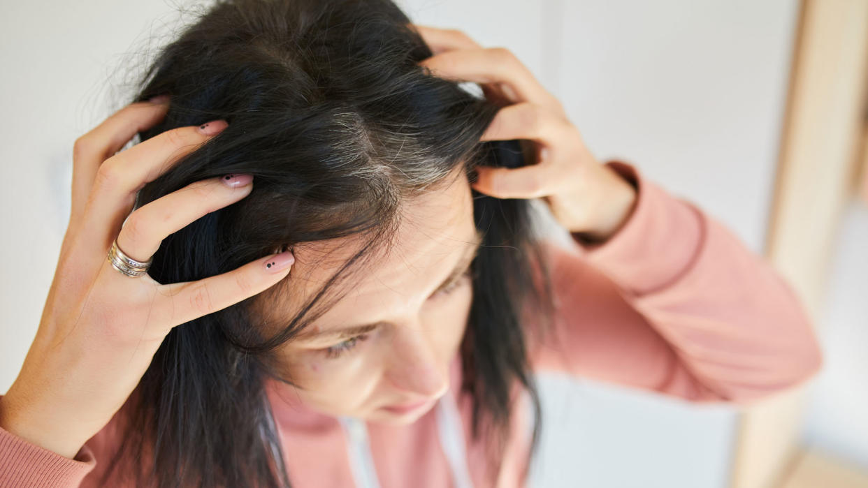  woman inspecting grey  heads along her hairline 