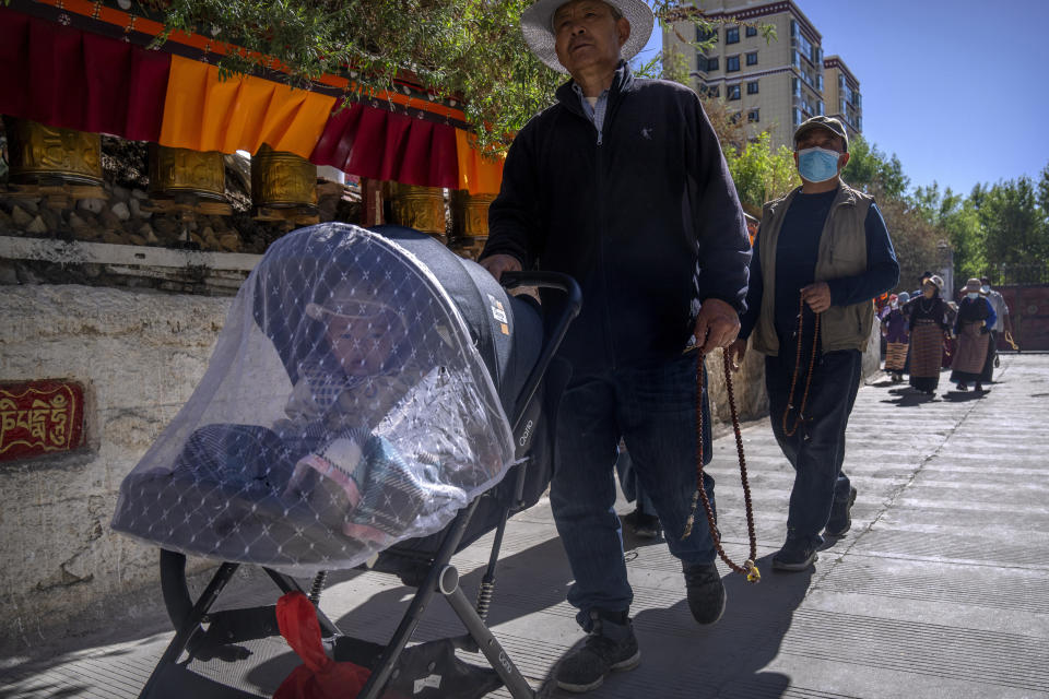 A man holds prayer beads and pushes a child in a stroller as he circumambulates around a neighborhood Tibetan Buddhist shrine in the Chengguan district of Lhasa in western China's Tibet Autonomous Region, as seen during a rare government-led tour of the region for foreign journalists, Thursday, June 3, 2021. Long defined by its Buddhist culture, Tibet is facing a push for assimilation and political orthodoxy under China's ruling Communist Party. (AP Photo/Mark Schiefelbein)