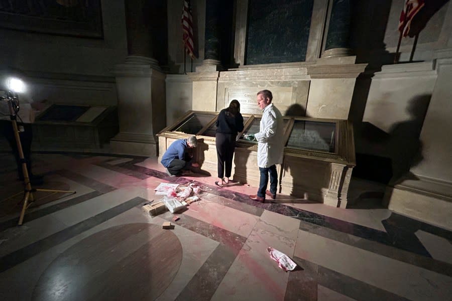 National Archives employees clean pink powder on the casement of the U.S. Constitution inside the National Archives Rotunda in Washington, Feb. 14, 2024. The National Archives building and galleries were evacuated after two protesters dumped powder on the protective casing around the U.S. Constitution. (Ellis Brachman/National Archives via AP)
