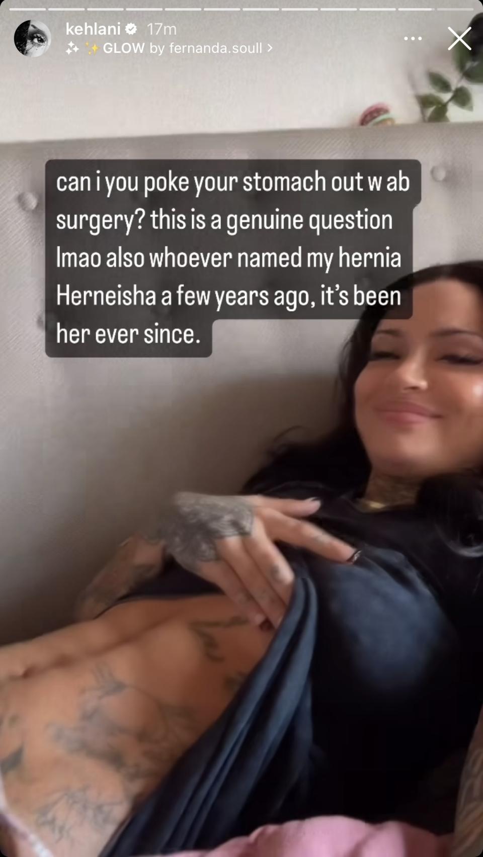 Smiling Kehlani lounging, with tattooed arm resting on torso and caption: "can i poke your stomach out w ab surgery? this is a genuine question lmao also whoever named my hernia Herneisha a few years ago, it's been her ever since"