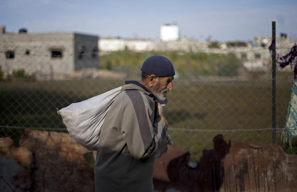 FILE - In this Dec. 25, 2013 file photo, a Palestinian man carries a sack of food as he walks in the Jabalya refugee camp in the northern Gaza Strip. Tens of thousands of Palestinians are no longer getting food aid or health services from America after the Trump administration’s decision in 2018 to cut more than $200 million in aid to the Palestinians. Before the aid cuts were announced, it provided food aid -- branded as a gift from the American people -- to more than 180,000 Palestinians in the Israeli-occupied West Bank and Gaza on behalf of the World Food Program. (AP Photo/Khalil Hamra, File)