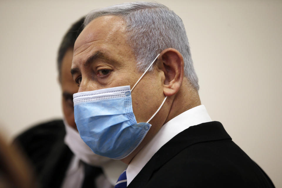 Israeli Prime Minister Benjamin Netanyahu, wearing a face mask in line with public health restrictions due to the coronavirus pandemic, stands inside the court room as his corruption trial opens at the Jerusalem District Court, Sunday, May 24, 2020. He is the country’s first sitting prime minister ever to go on trial, facing charges of fraud, breach of trust, and accepting bribes in a series of corruption cases stemming from ties to wealthy friends. (Ronen Zvulun/ Pool Photo via AP)