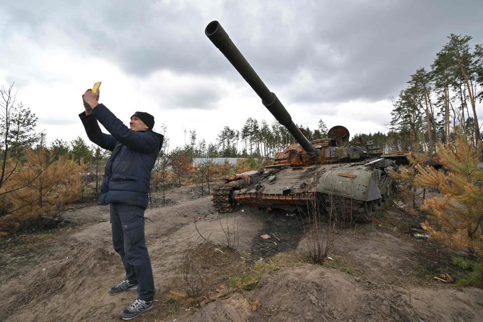 A man takes a selfie as he stands in front of a destroyed Russian tank in the vilage of Andriivka, in the Kyiv region on April 17, 2022.