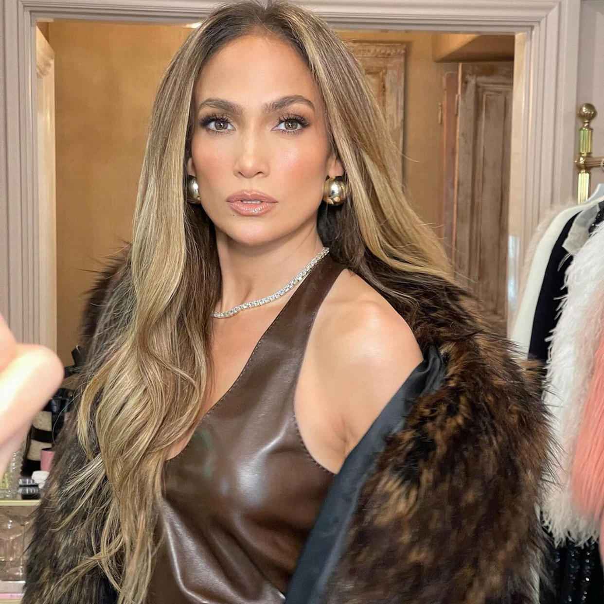  Jennifer Lopez wearing an all-brown outfit with a fur coat while posing in her closet. 