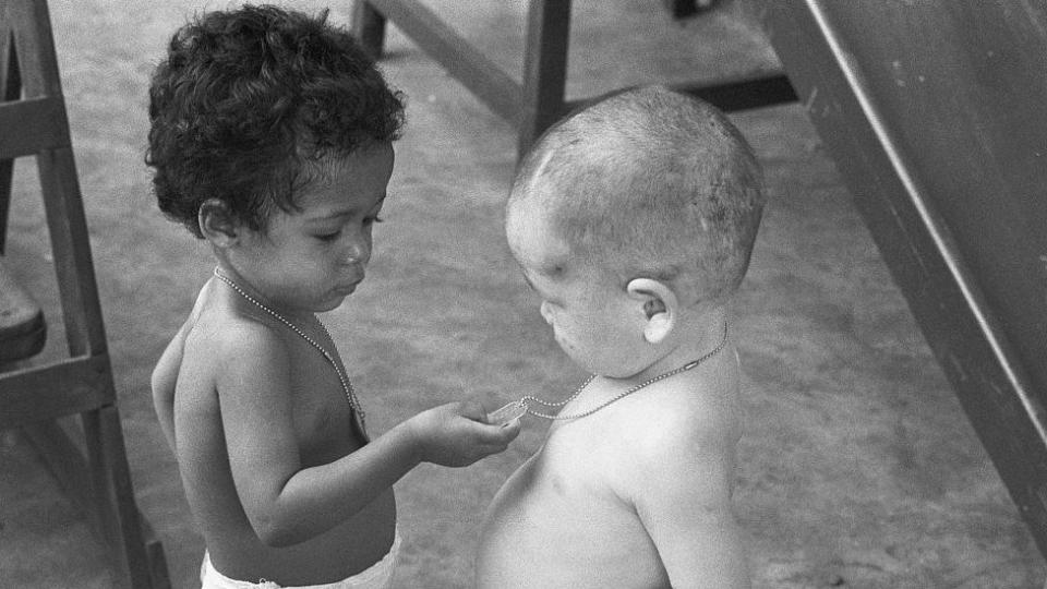 Niños mitad estadounidenses, mitad vietnamitas mirando los "dog tags" que les cuelgan del cuello.