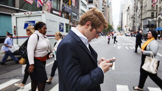 A man uses his Apple iPhone while walking across 5th Avenue in New York