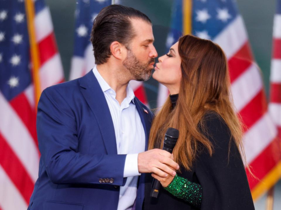 Donald Trump Jr. and Kimberly Guilfoyle kiss with American flags in the background