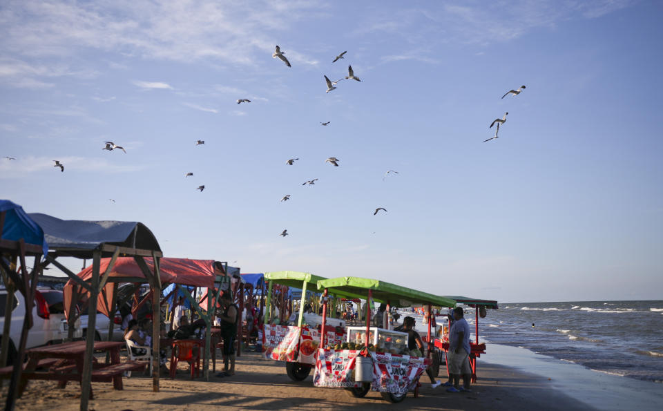 In this Aug. 2, 2019 photo, seagulls fly over food trucks in Playa Bagdad close to the mouth of the Rio Grande, near the border city of Matamoros, Mexico. Unlike the Tijuana-Imperial beach border, on the western end, here there are no steel pilings marching out to sea, to stop migrants from swimming, wading or paddling across to the United States. (AP Photo/Emilio Espejel)