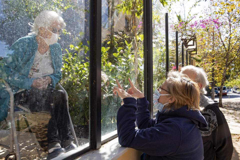 Yara Loureiro, right, speaks with her 90-year-old mother Lourdes Giannini through a glass window at the Premier Hospital, where her mother is a patient after suffering a stroke, in Sao Paulo, Brazil, Tuesday, May 26, 2020. The hospital does not have any cases of COVID-19, but has closed visits to patients to prevent contagion of the new coronavirus. (AP Photo/Andre Penner)