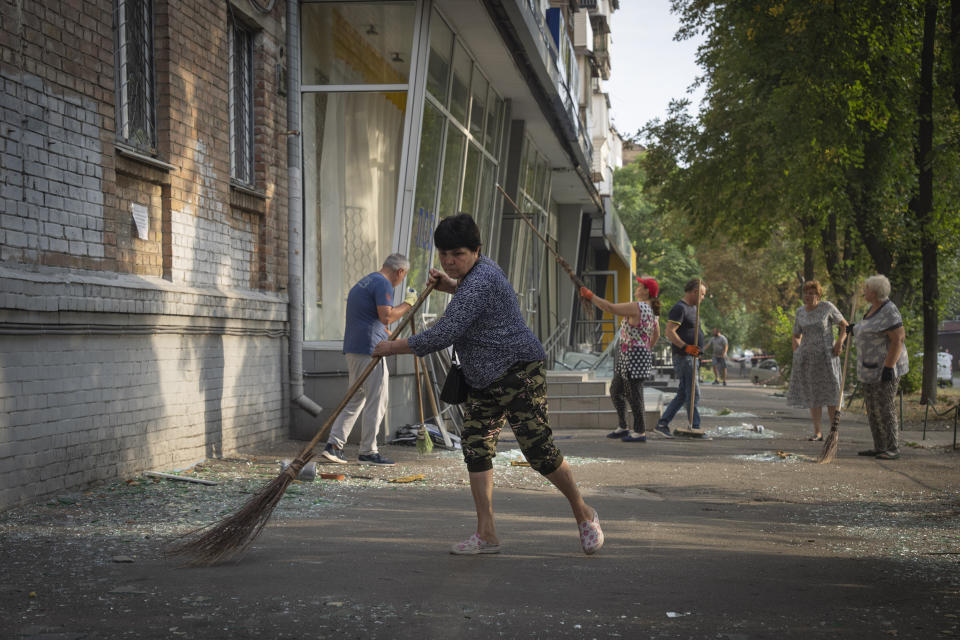 Local residents clean the street from broken glass that fell down from the windows of their apartments and shops after Russian rocket attack in Kyiv, Ukraine, Wednesday, Aug. 30, 2023. Over 20 rockets and drones have been shot down by the air defence system in Kyiv overnight. (AP Photo/Efrem Lukatsky)