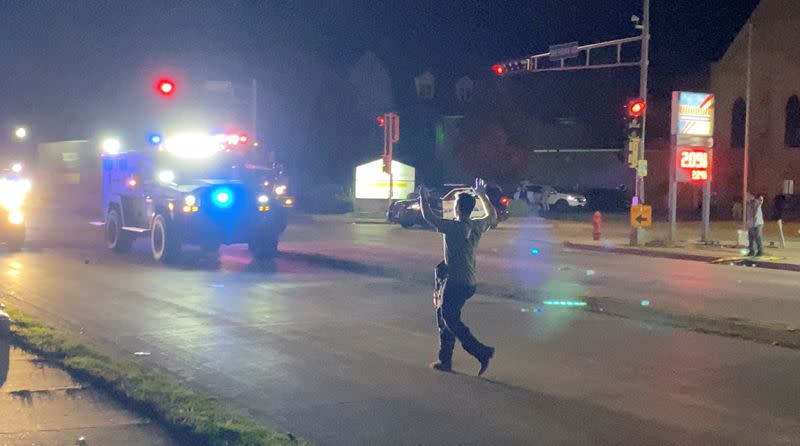 A man with a firearm raises his hands up as he walks towards vehicles during a protest following the police shooting of Jacob Blake, a Black man, in Kenosha