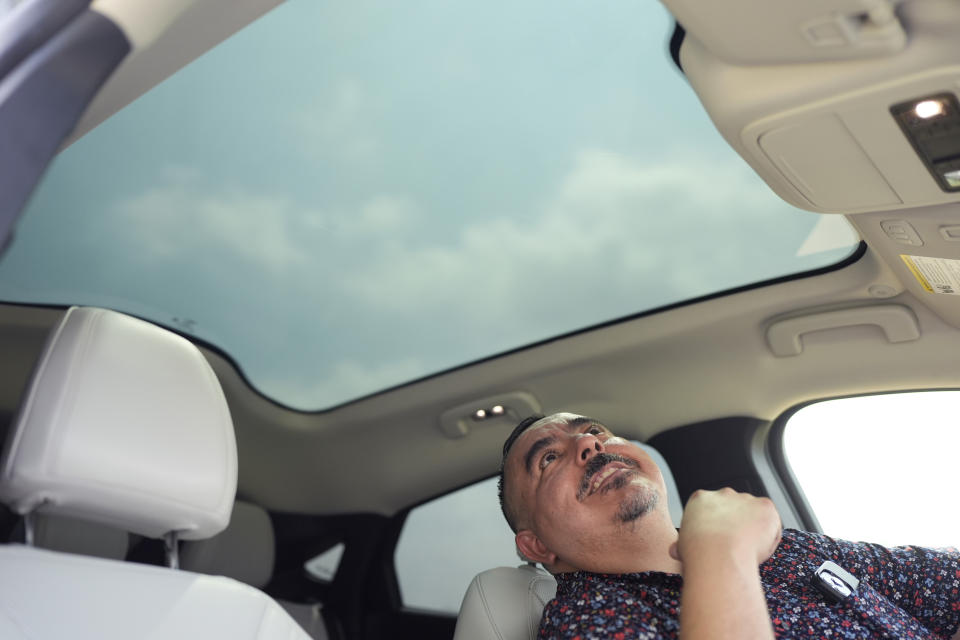 Jose Valdez, 45, who owns three EVs, looks through the panoramic roof of his Mustang Mach-E, Thursday, May 9, 2024, in San Antonio. Many Americans still aren’t sold on going electric for their next car purchase. High prices and a lack of easy-to-find charging stations are major sticking points, a new poll shows. Valdez owns three EVs, including a new Mustang Mach-E. With a tax credit and other incentives, the sleek new car cost about $49,000, Valdez said. He thinks it's well worth the money. (AP Photo/Eric Gay)