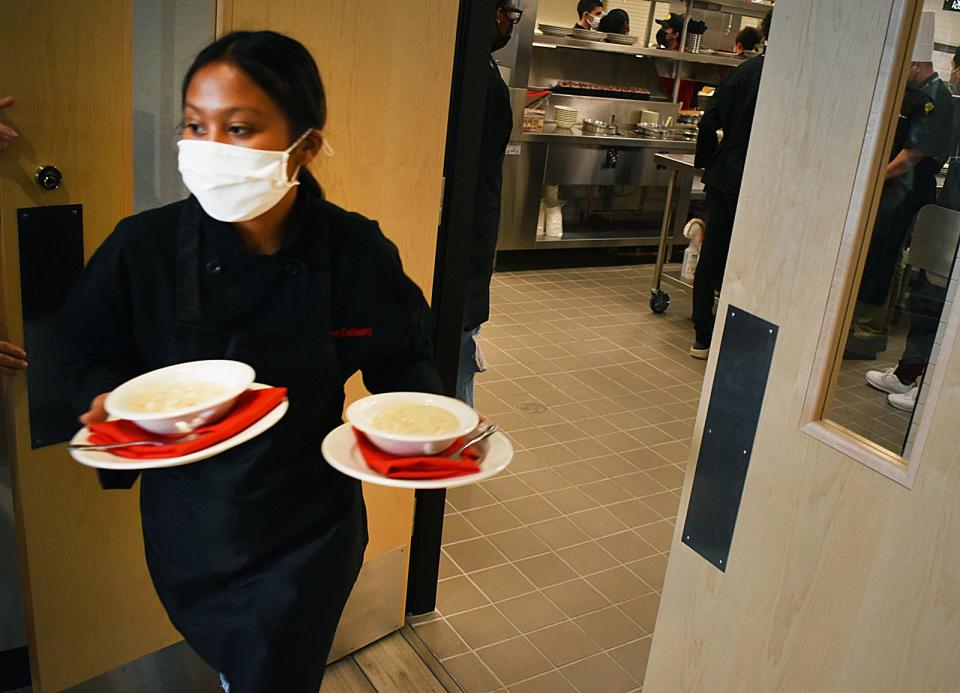 Server Osaphea Chin, a senior at Durfee High School in Fall River, carries orders out of the kitchen at the school's restaurant, Granite Grille.